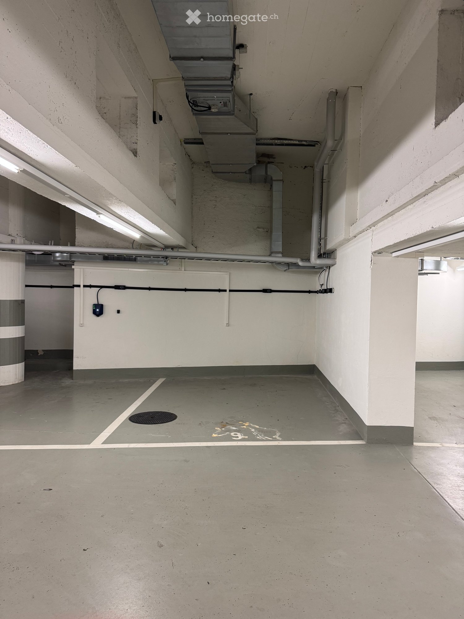 Unfurnished Room. Empty underground parking area with concrete floors, white walls, and visible pipes and electrical equipment.