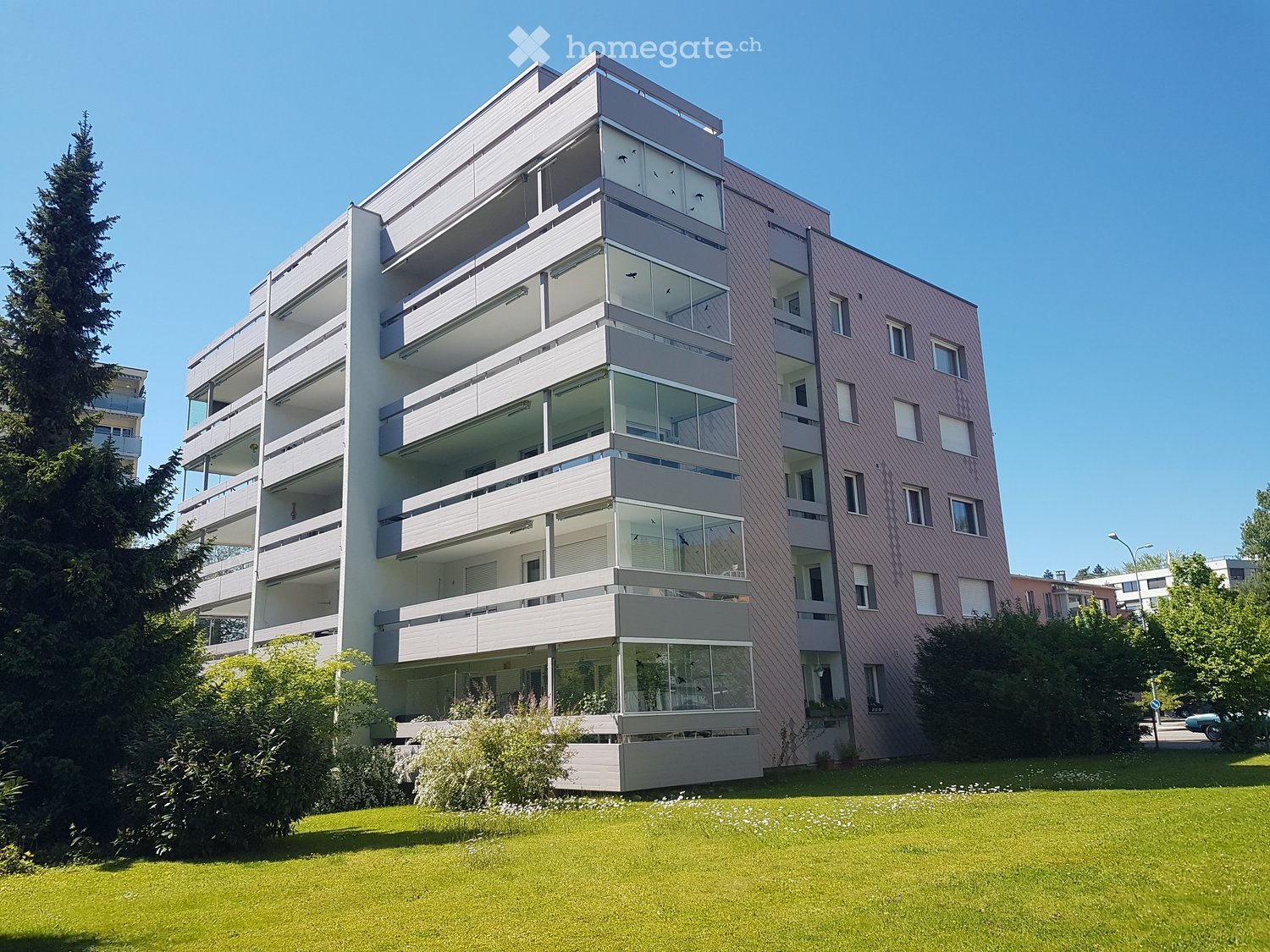modern apartment building, multiple balconies, glass windows, green lawn, trees
