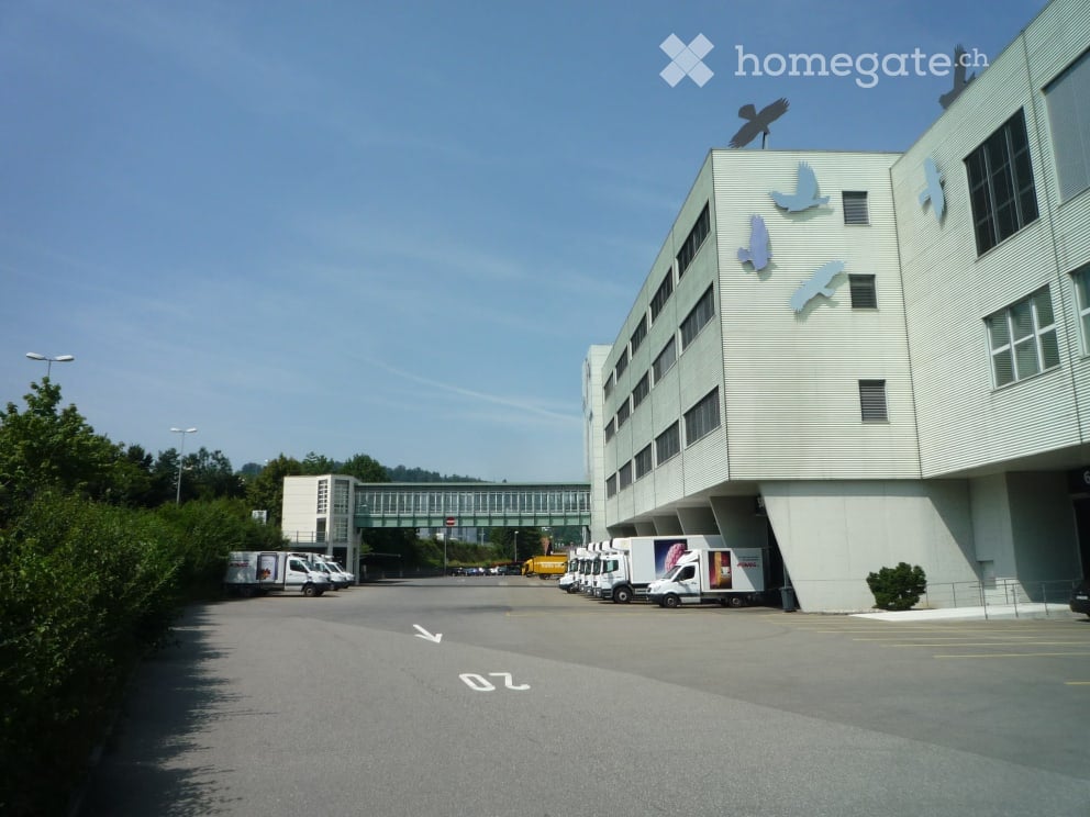 commercial building, several delivery trucks parked in front, trees, bridge in the background