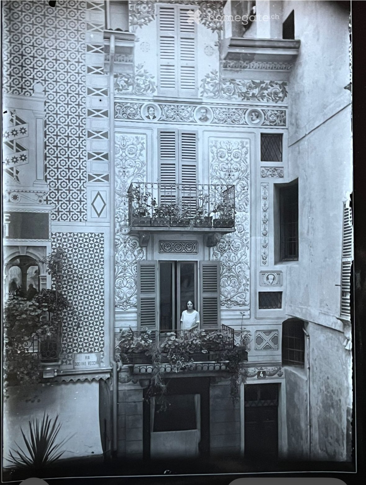 balcony with railings, decorative floral patterns, woman in white shirt standing by window