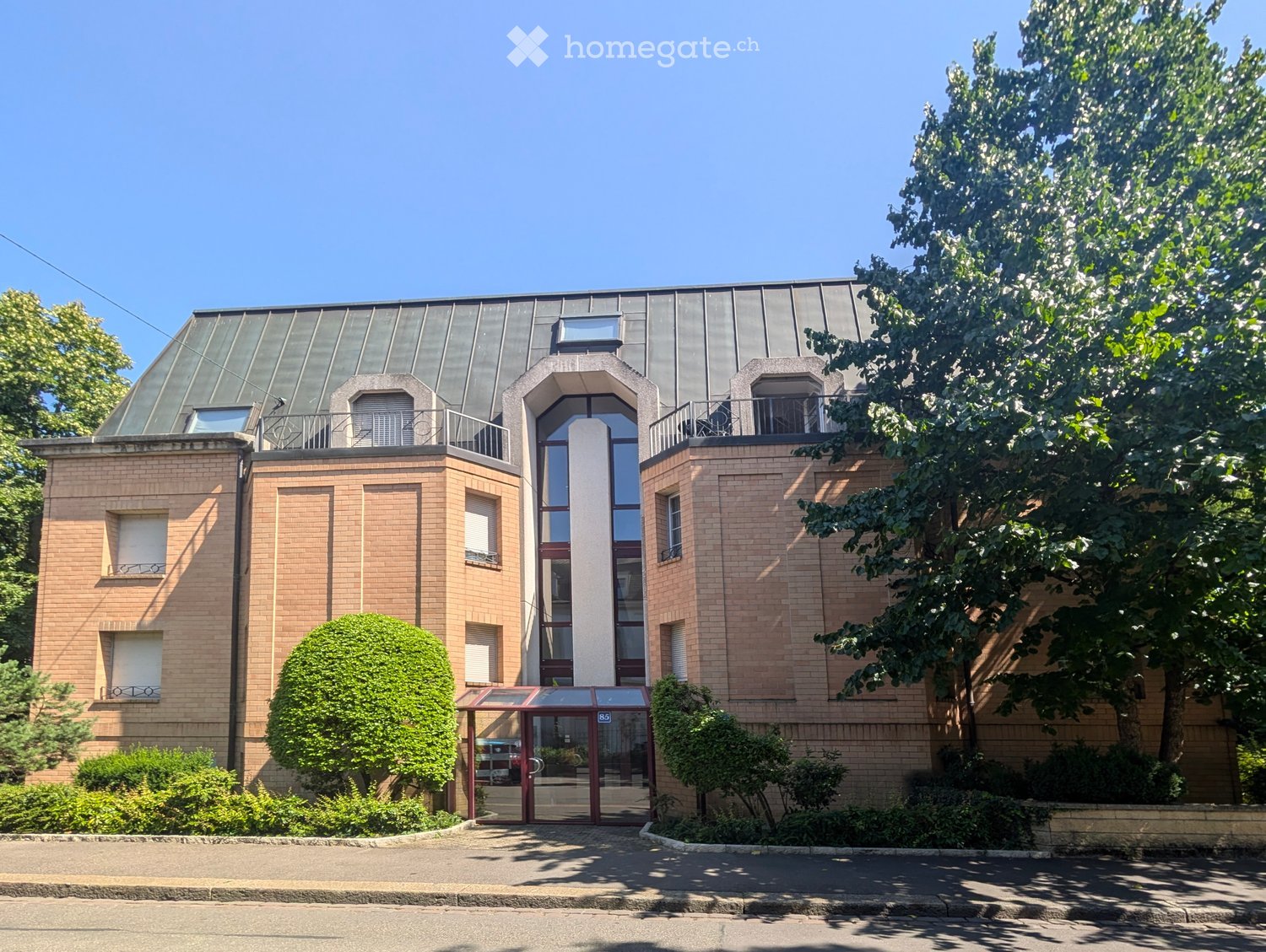3 story building, brick walls, glass windows, glass entrance, metal roof, front garden