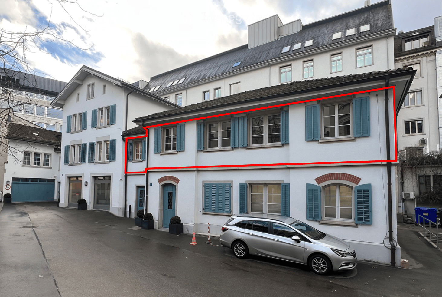 White apartment building, white walls, blue shutters, a car is parked in front of the entrance