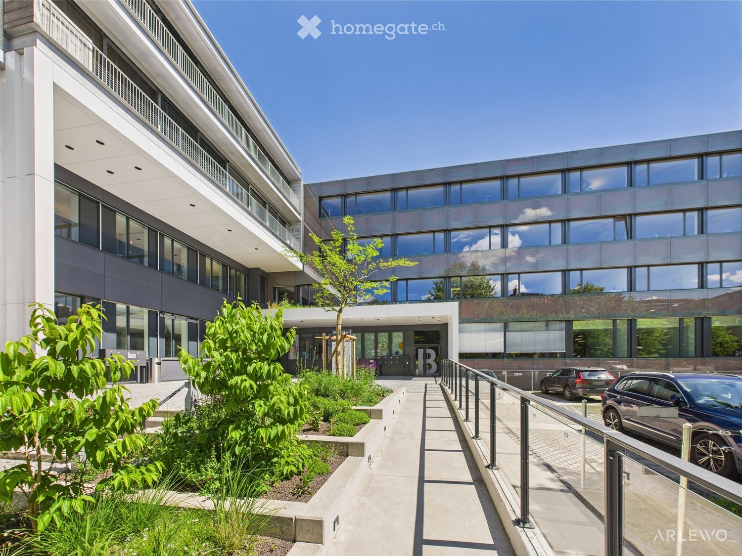 Modern office building with glass windows, landscaped entrance, and parking area.