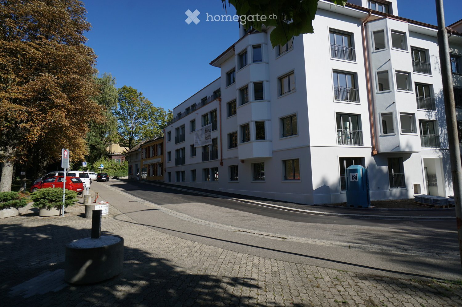 White residential building, multiple balconies, street parking
