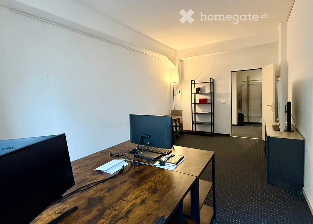 wooden desk, two monitors, keyboard and mouse, shelves, chairs, table lamp