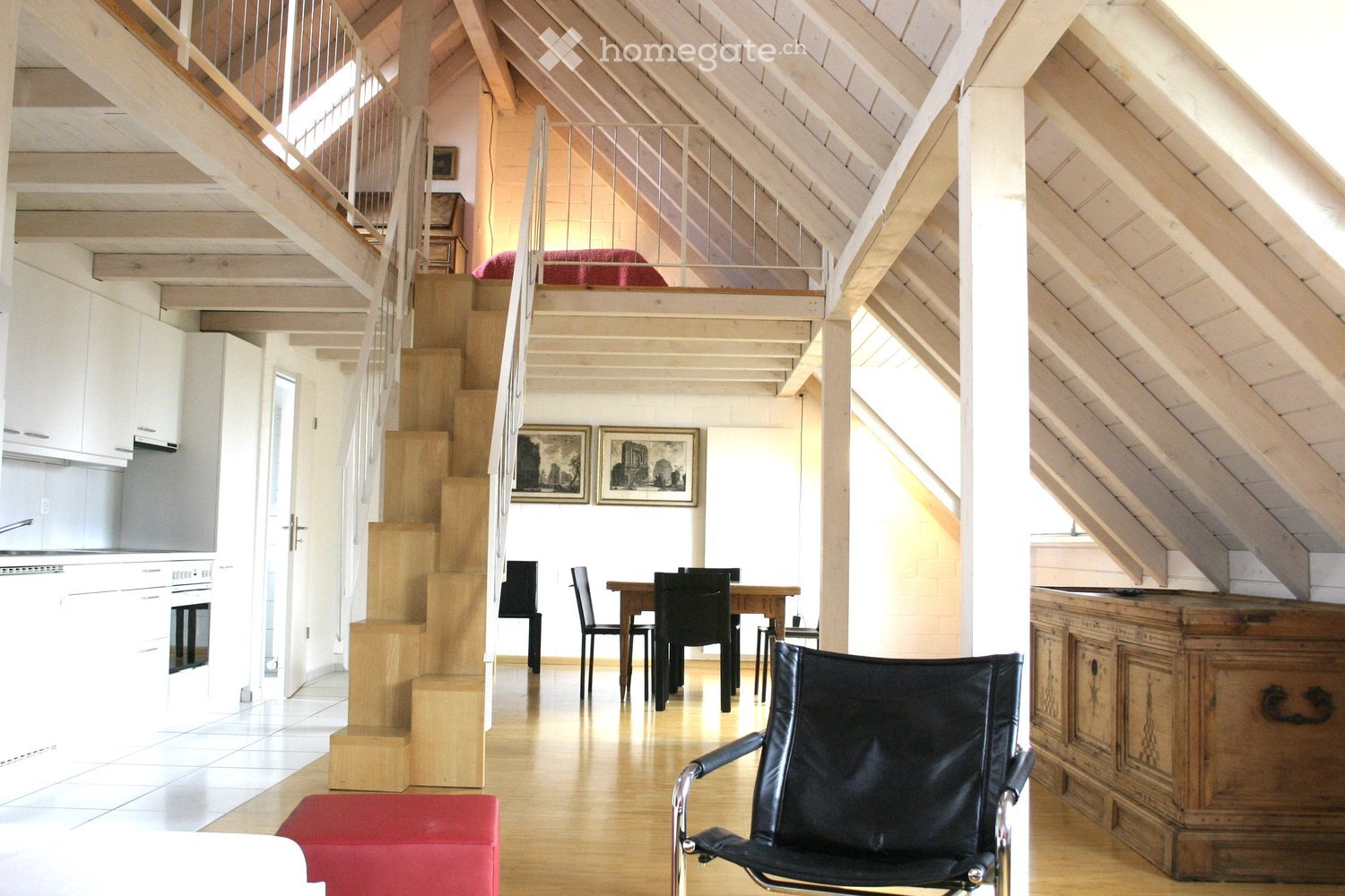 loft area with staircase, dining area, black leather chair, wooden dining table, white kitchen cabinets, red cushion on floor, picture frames on wall