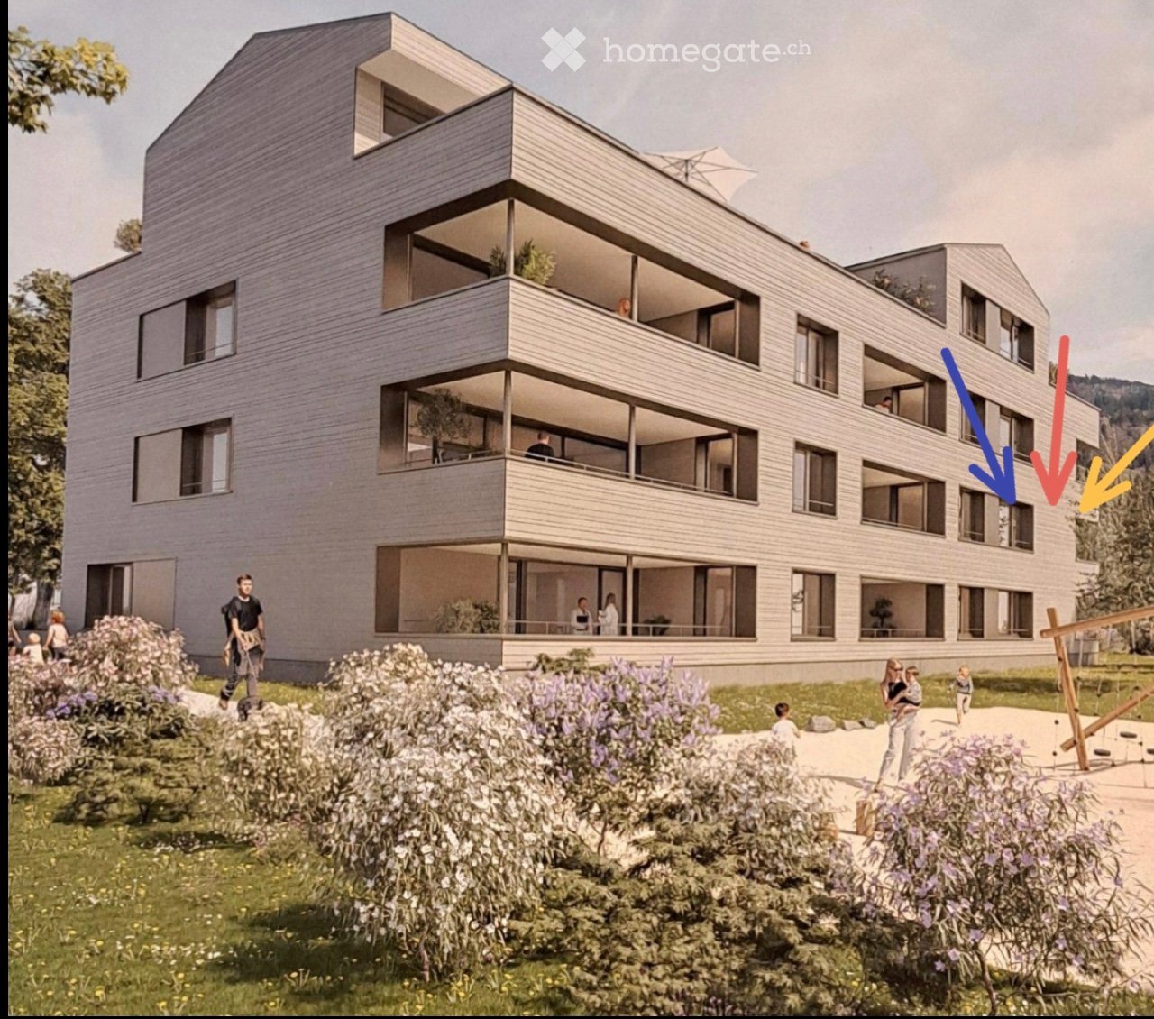 3 story building, grey exterior, balconies with railings, multiple windows, trees and plants surrounding the building, playground