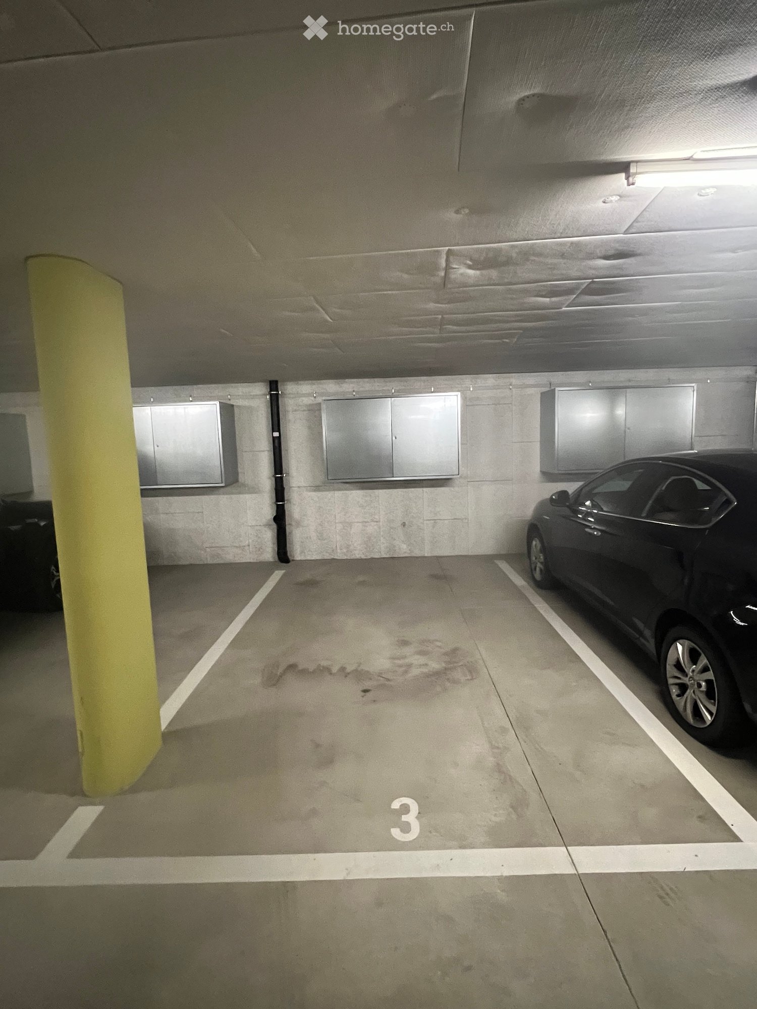 Number 3 parking spot in a covered underground garage, concrete walls, silver storage cabinets, yellow support pole, and a black car parked.