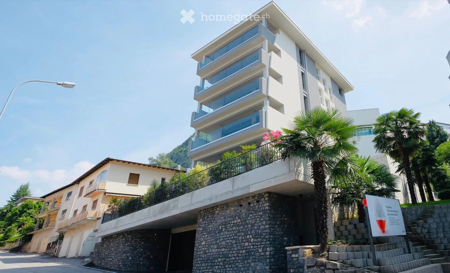 modern residential building with glass balconies, stone base, street lamp, stone stairs, greenery