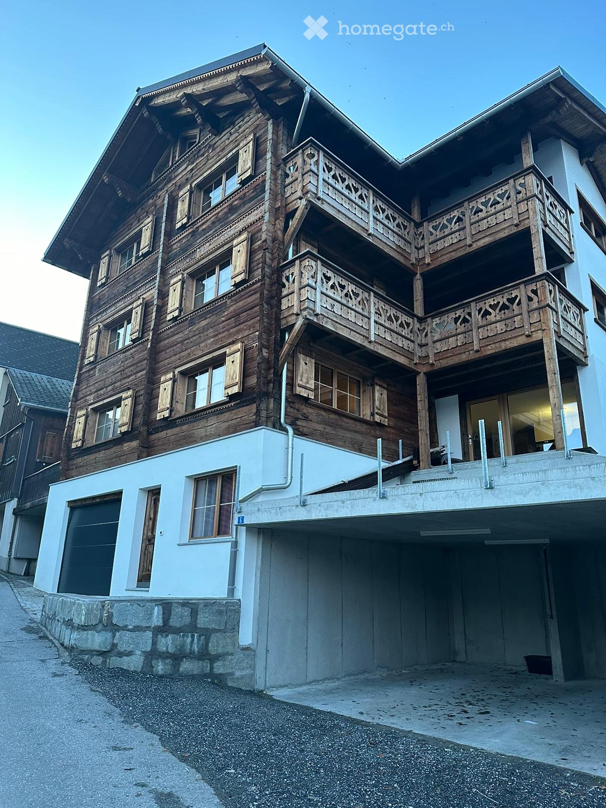4 story wooden chalet style building, wooden balconies, underground garage, white exterior ground floor, wooden shutters, many windows