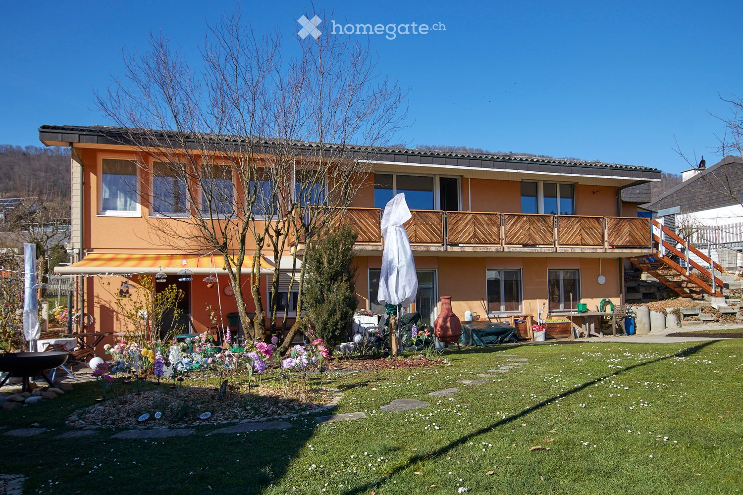 Two-story house, beige exterior, wooden balcony, wooden staircase, fenced garden, terrace, large windows