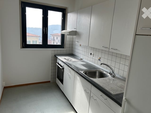 Clean kitchen with white cabinets, black countertop, sink, oven, window.