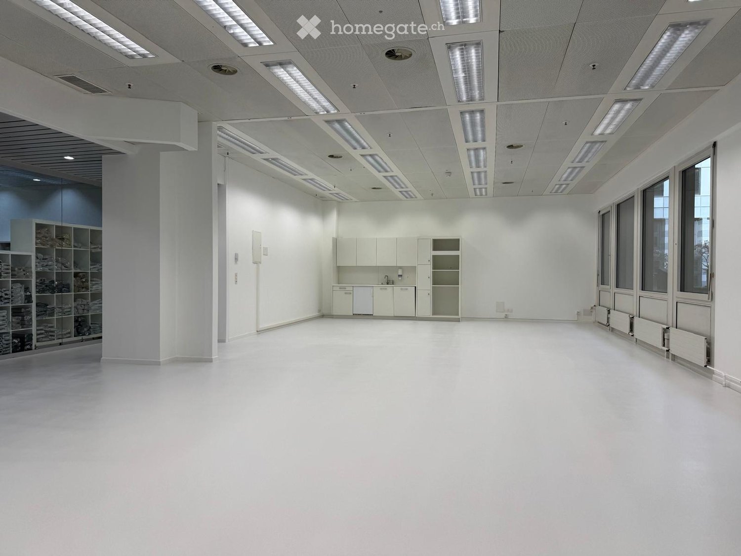 Spacious room, white walls and flooring, recessed ceiling lighting, built-in cabinets, glass windows, storage shelves