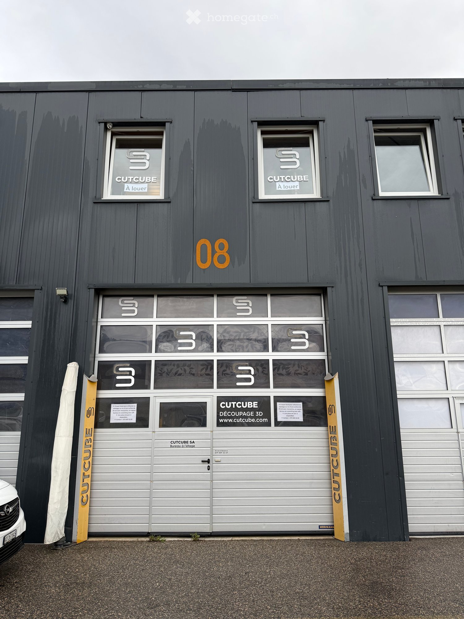 industrial style building, grey exterior, three windows, double garage doors, sign that says 'CUTCUBE'