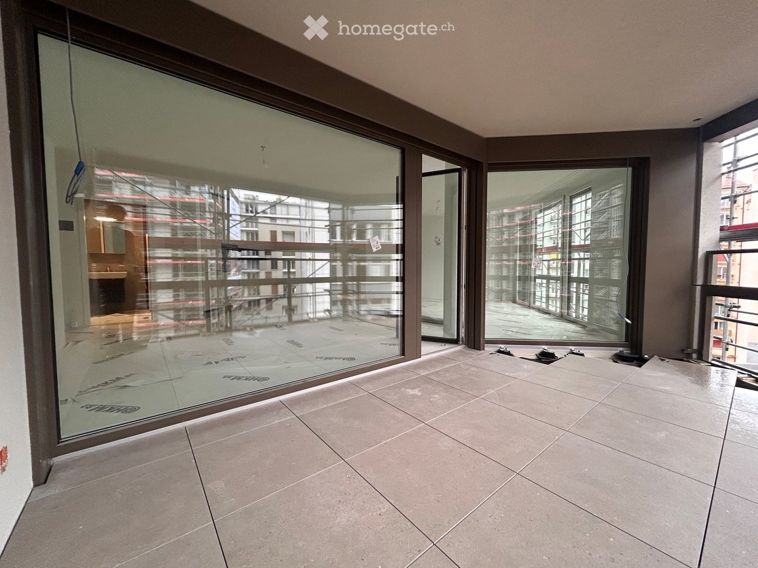 Empty room with tiled floor and large glass windows offering a view of the surrounding area.