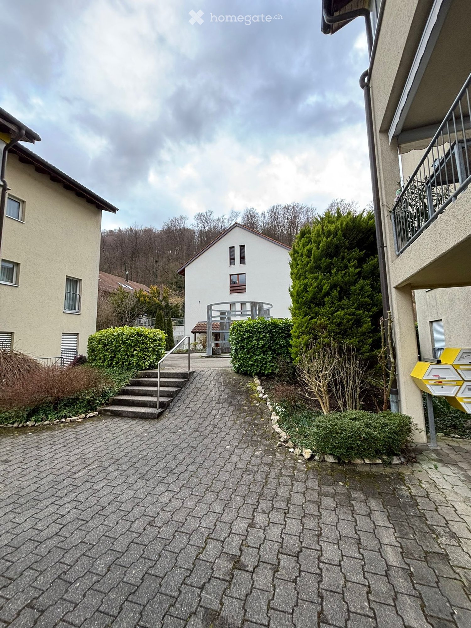 Two-story house, white exterior, brick walkway, stairs to entrance, shrubs and bushes, glass front