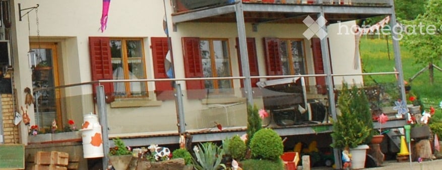 3 story house, white walls, red shutters, balcony, garden with potted plants and trees