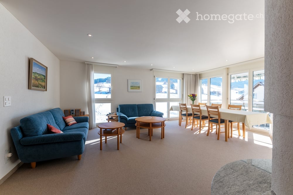 Living area with sofas, wooden tables, dining area with table and chairs, and large windows with view