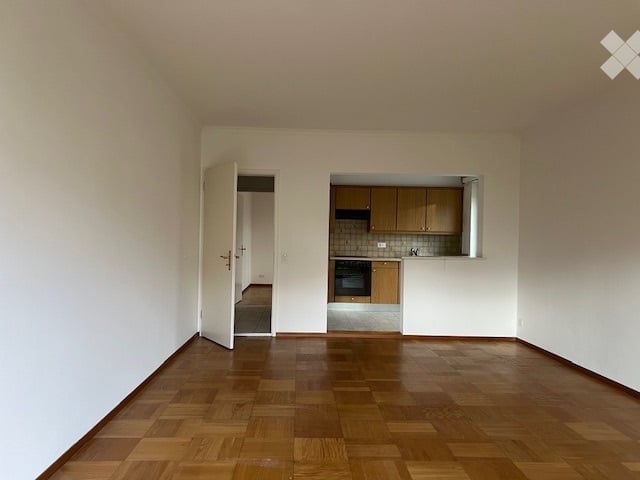 empty room with open door, wooden floor, kitchen with oven, kitchen island, kitchen cabinets