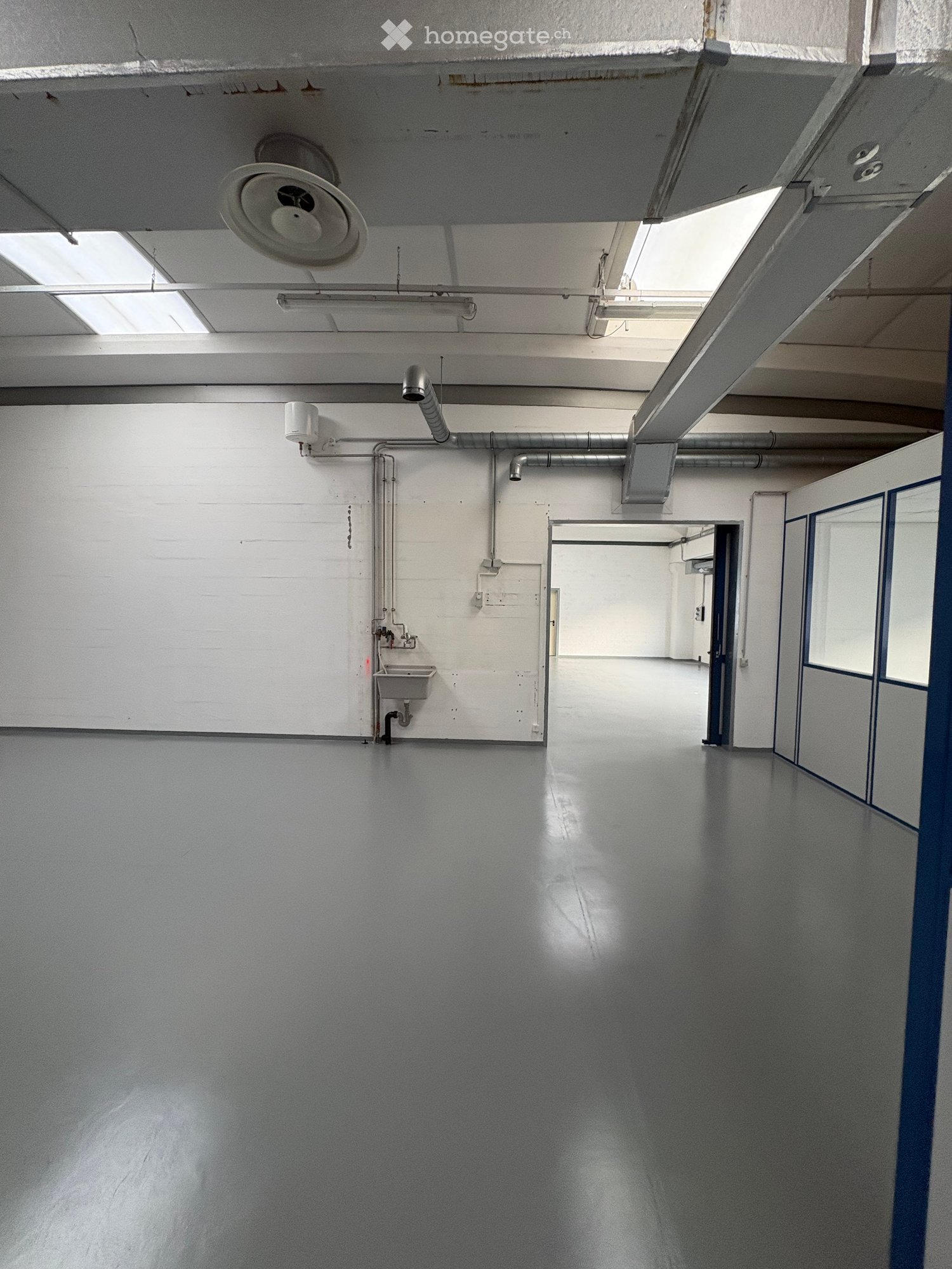 Empty room with white walls, gray floor, a sink, and pipes on the wall