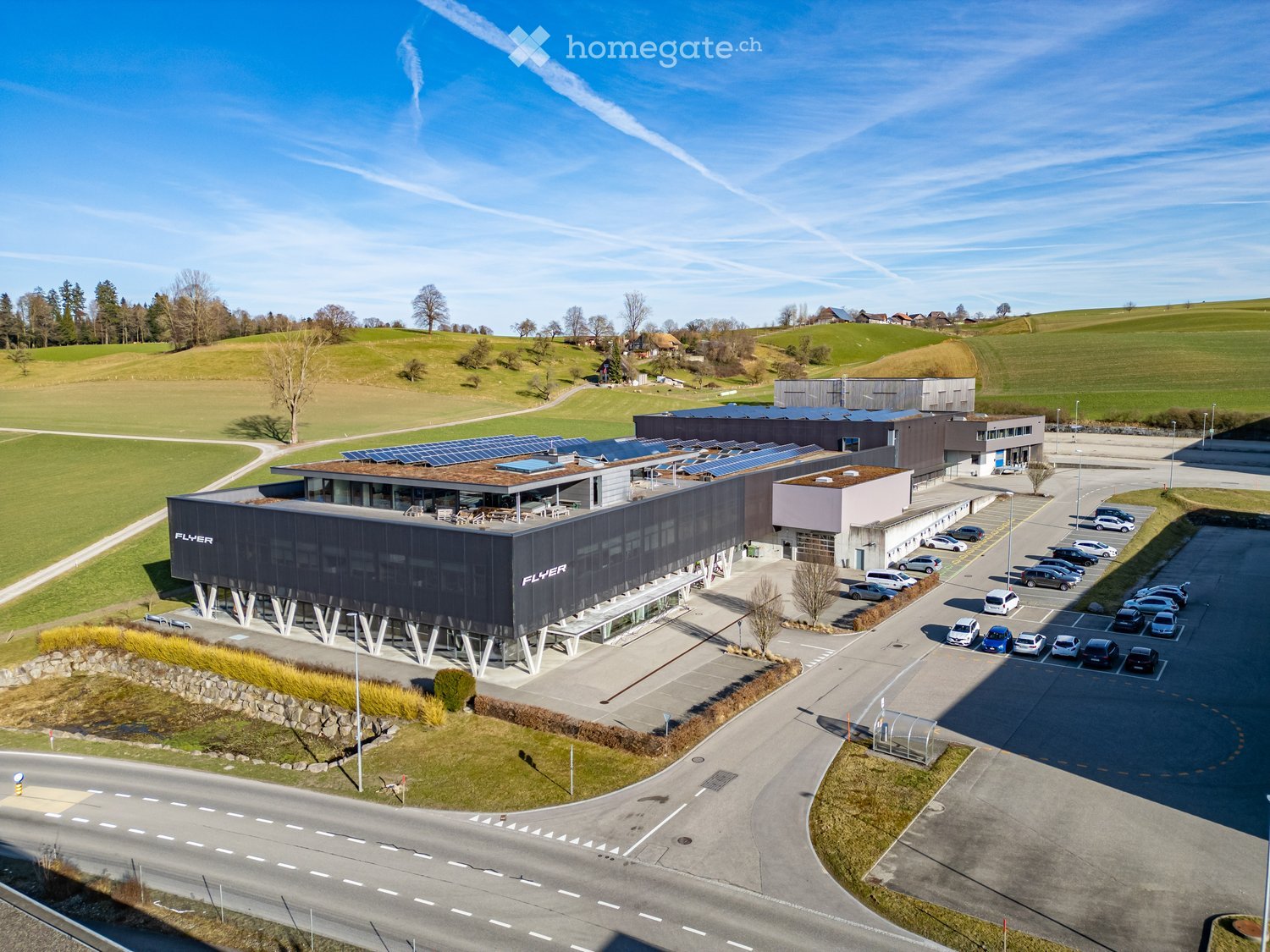 modern building with solar panels, large parking lot, surrounded by green fields