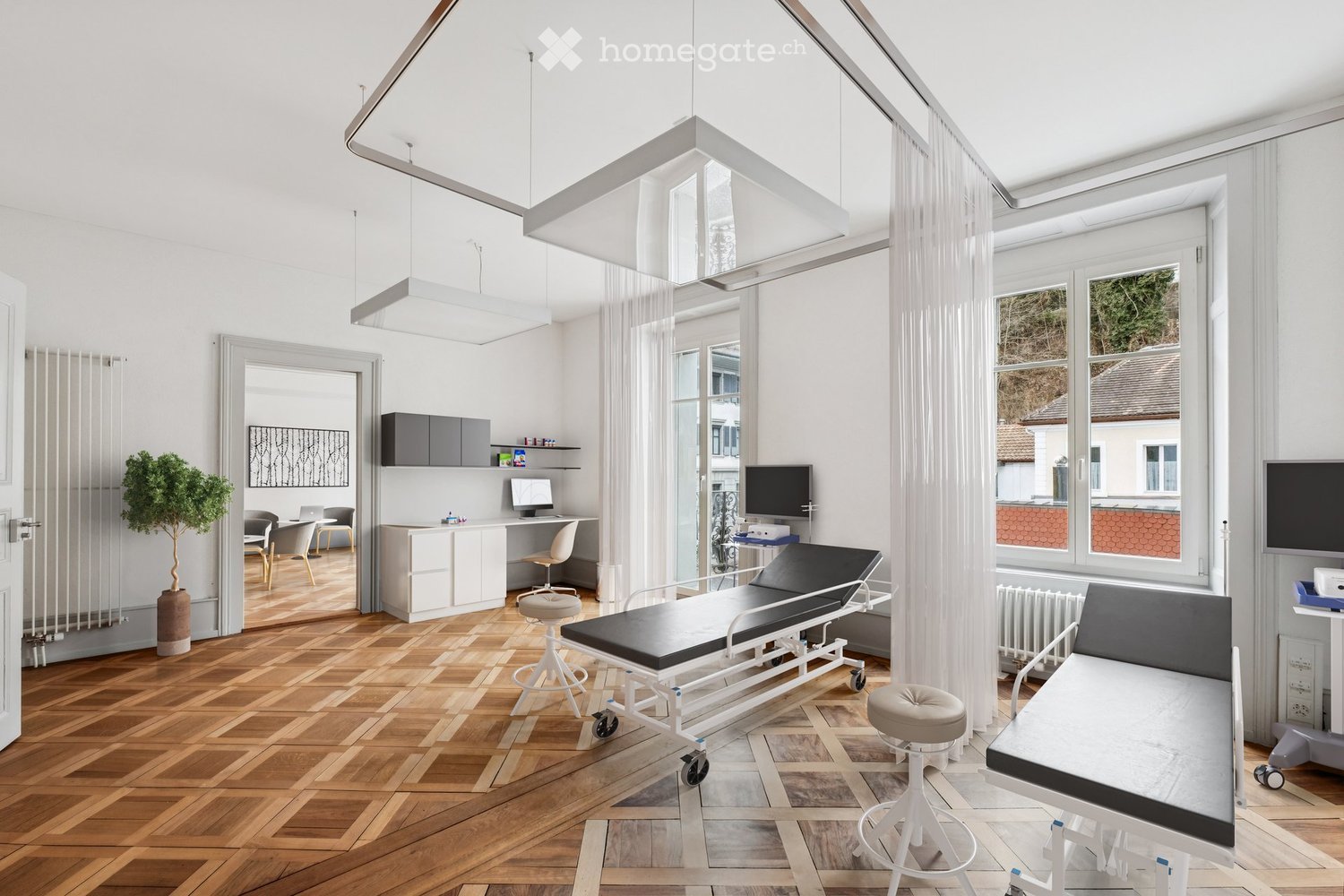 modern medical room with wooden floor, white walls, medical beds, desk, monitor, and a potted plant