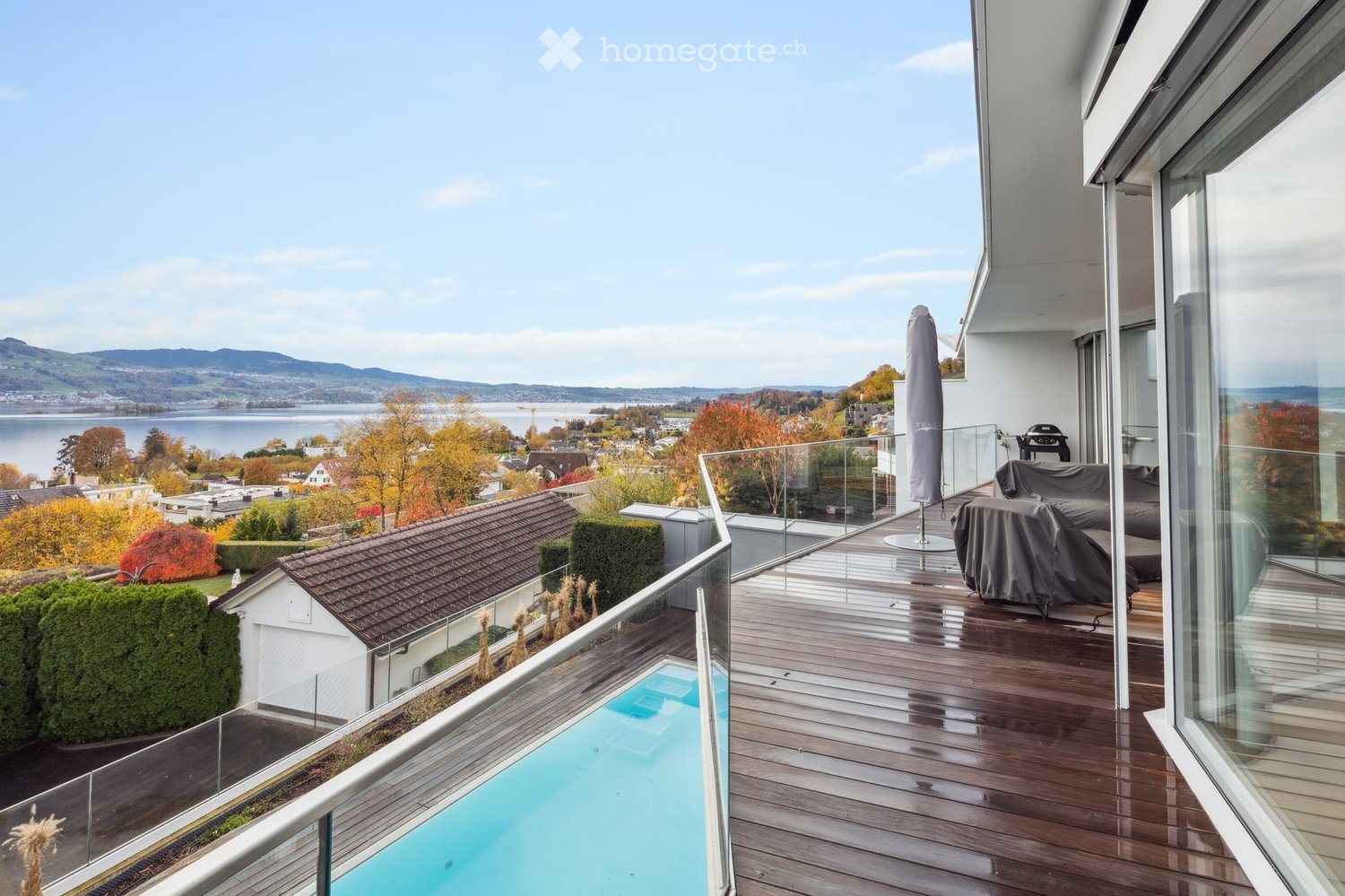 Balcony with wooden deck, glass railing, swimming pool, lake view, mountain view