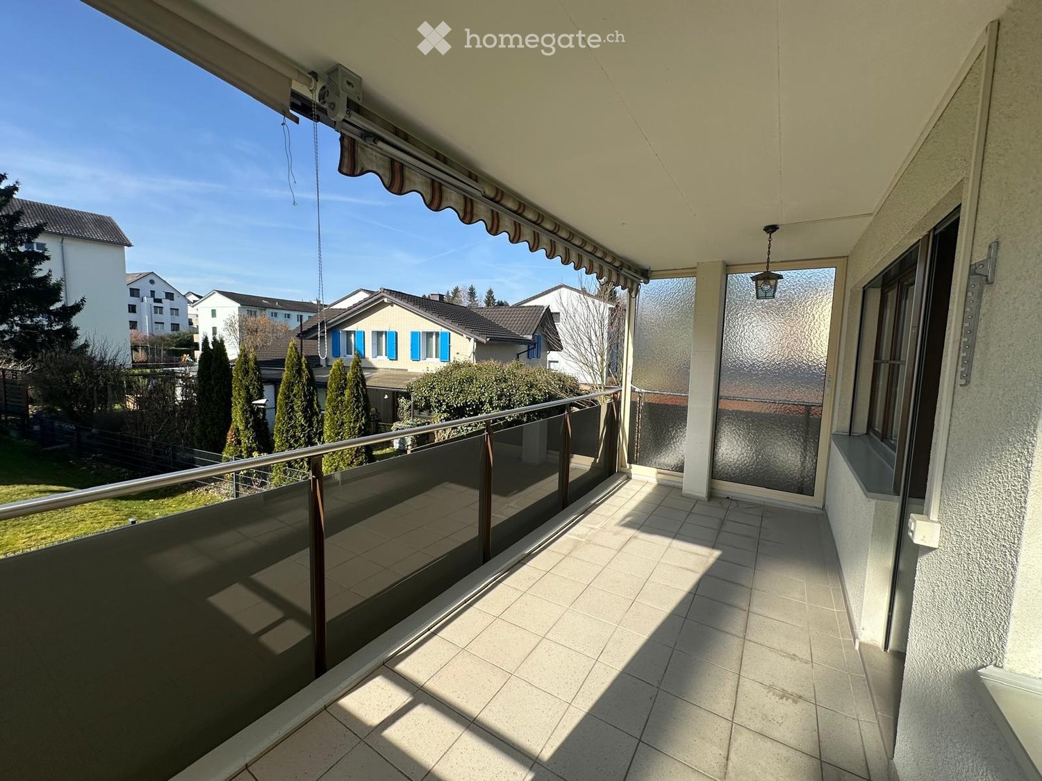 spacious balcony, tiled floor, metal railing, retractable awning, hanging lantern, open door, sunny