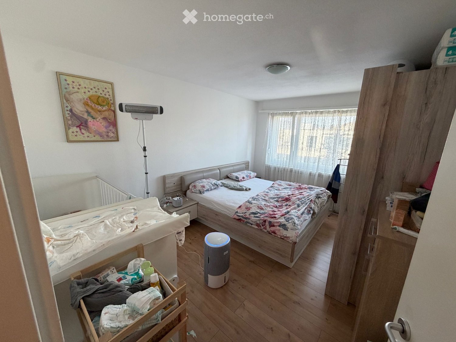 Bedroom with bed, nightstand, lamp, air purifier, wooden floor, wooden cabinet, painting, crib, and storage box