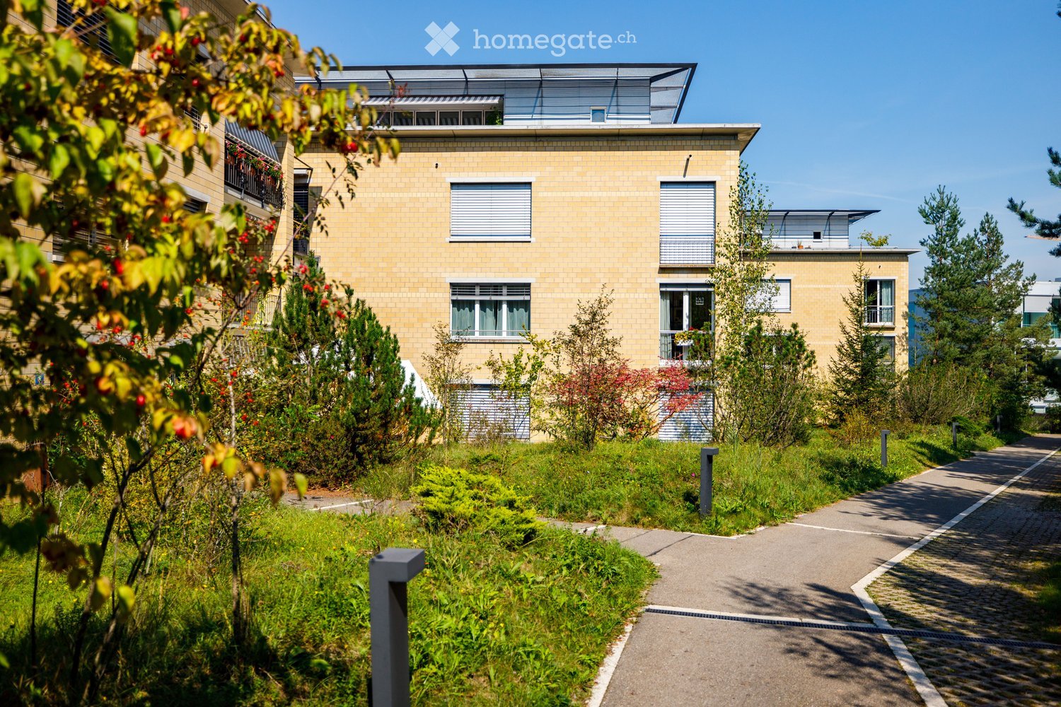 multi-story building, brick walls, multiple windows, balconies with railings, small garden in front