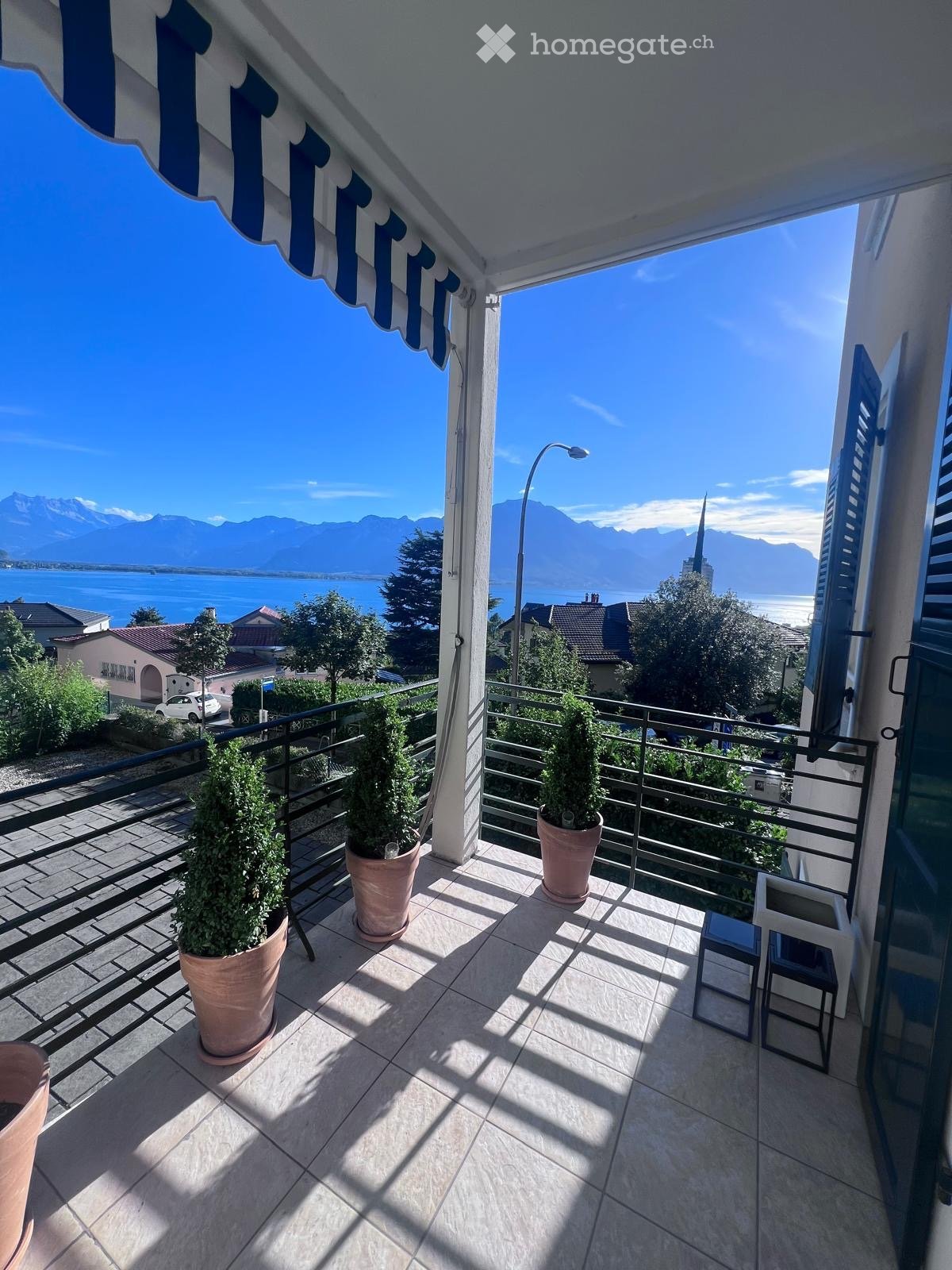 tiled floor, black railing, 3 potted plants, view of mountains and lake