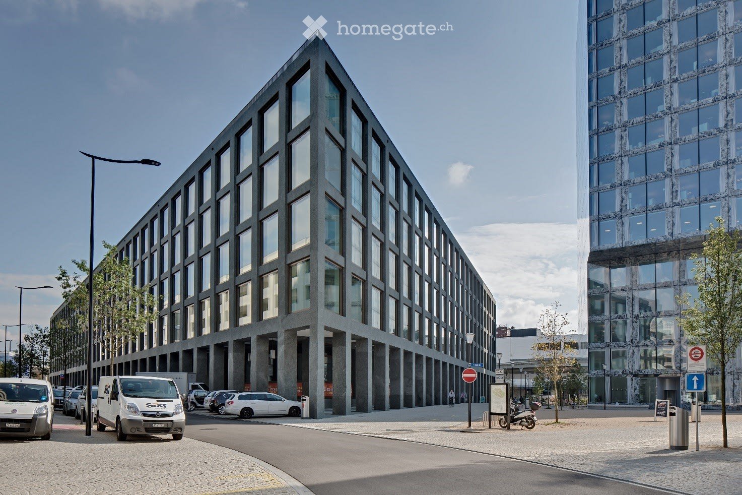 Modern office building with glass facade, multiple floors, cars parked outside, street lights, paved street