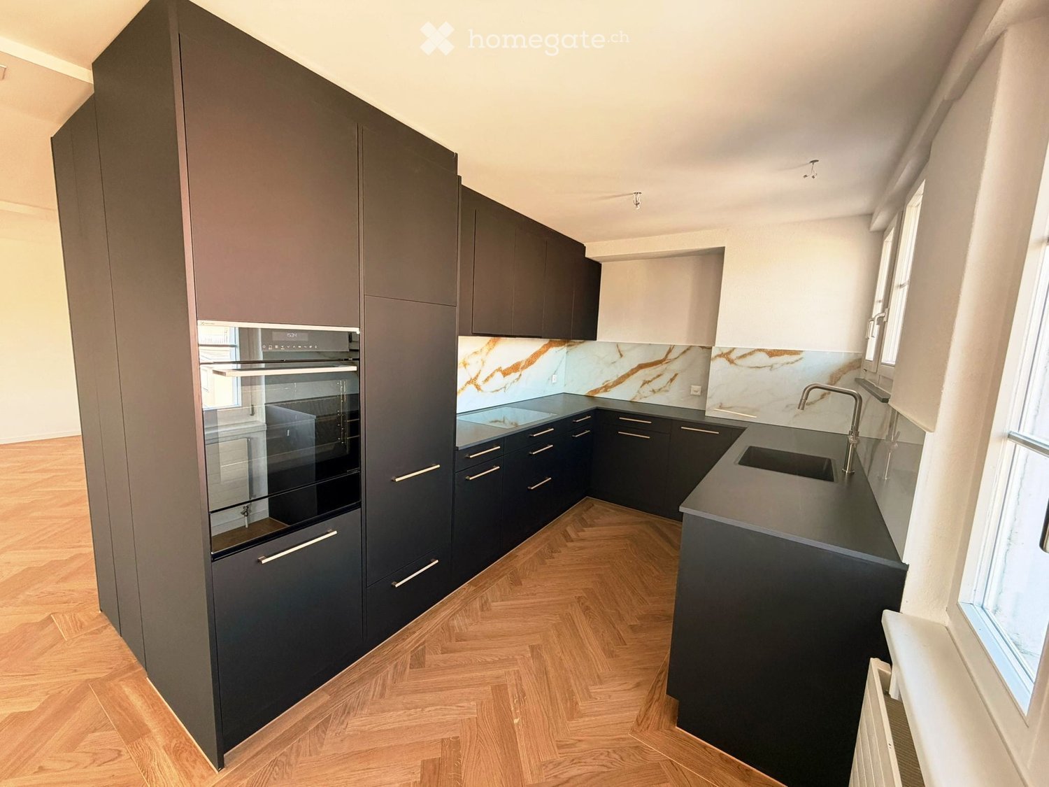 modern kitchen with black cabinets, wooden floor, marble countertops, stainless steel sink, oven, and faucet