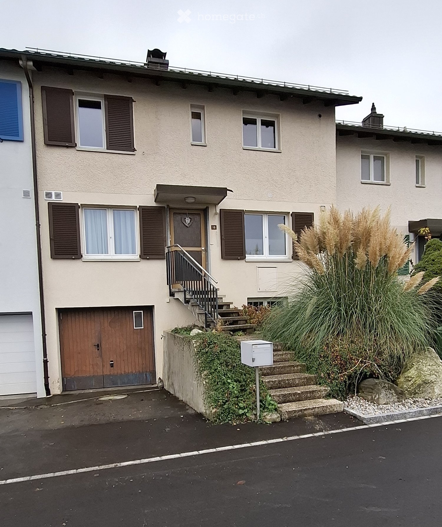 3 story house, beige walls, brown wooden doors, 2 garages, stairs to the entrance