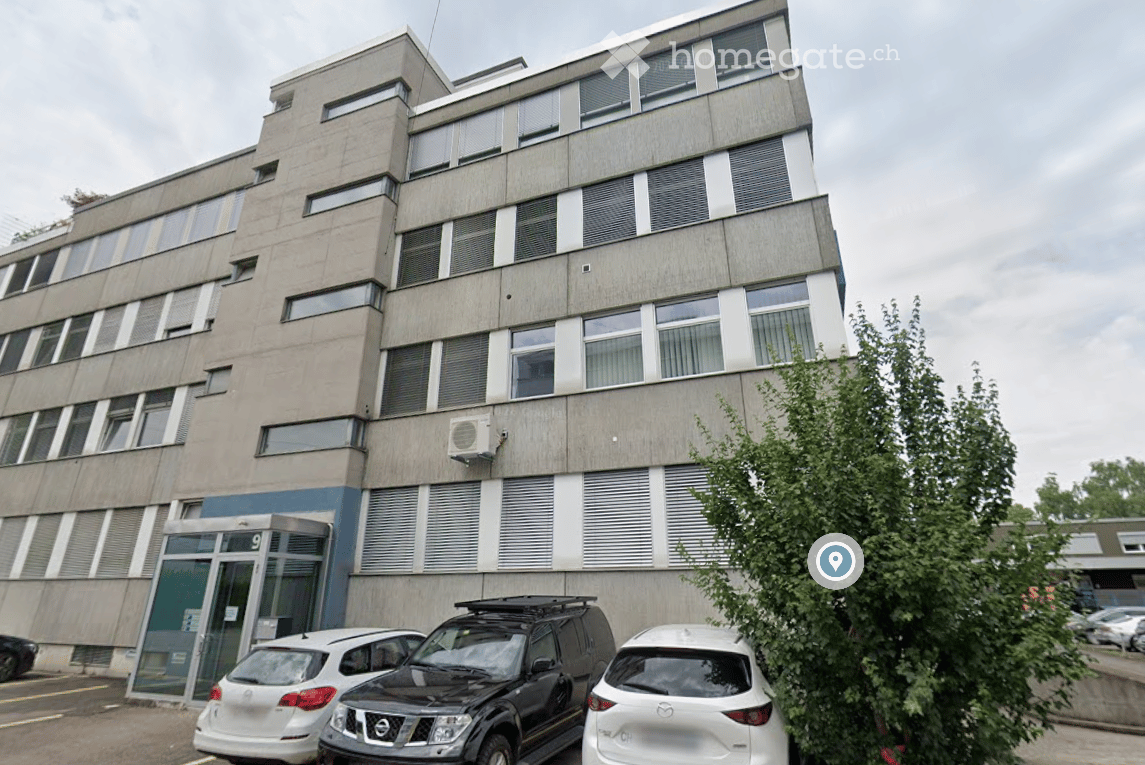 multi-story building, grey exterior, multiple windows, air conditioning unit, parking lot, cars parked