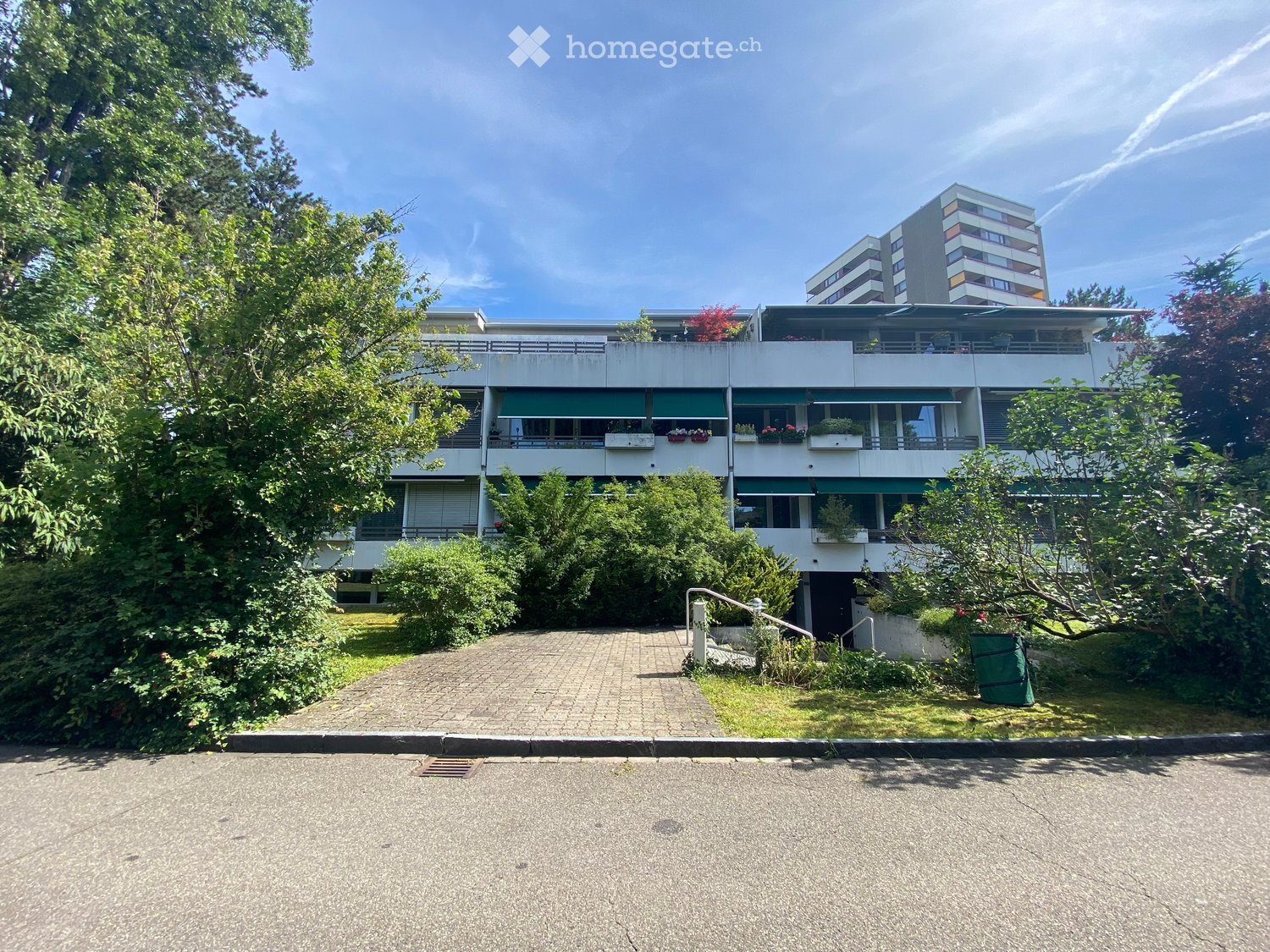 3 story apartment building, white exterior, green awnings, balconies, trees, shrubs, paved driveway