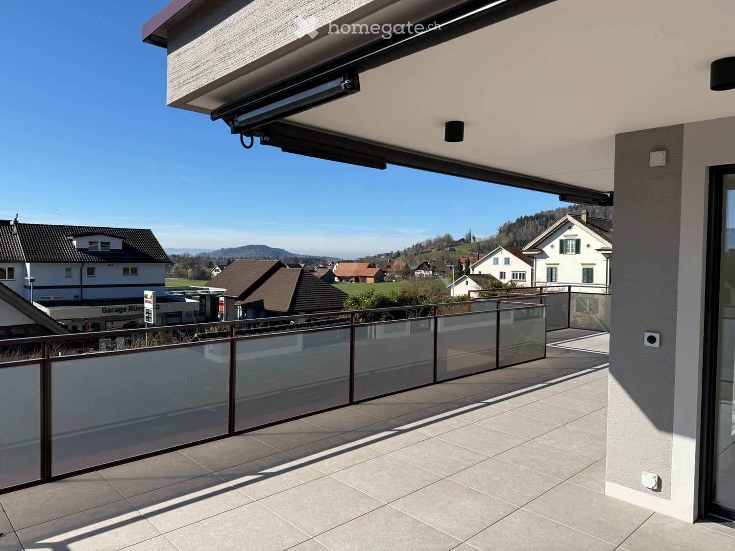 large balcony with glass railing, tiled floor, view of the town