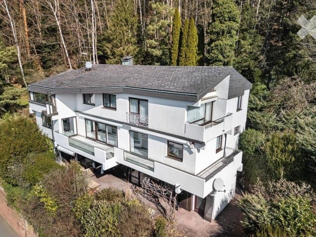 2-story house with a gray exterior, large windows, and a balcony overlooking a forested area