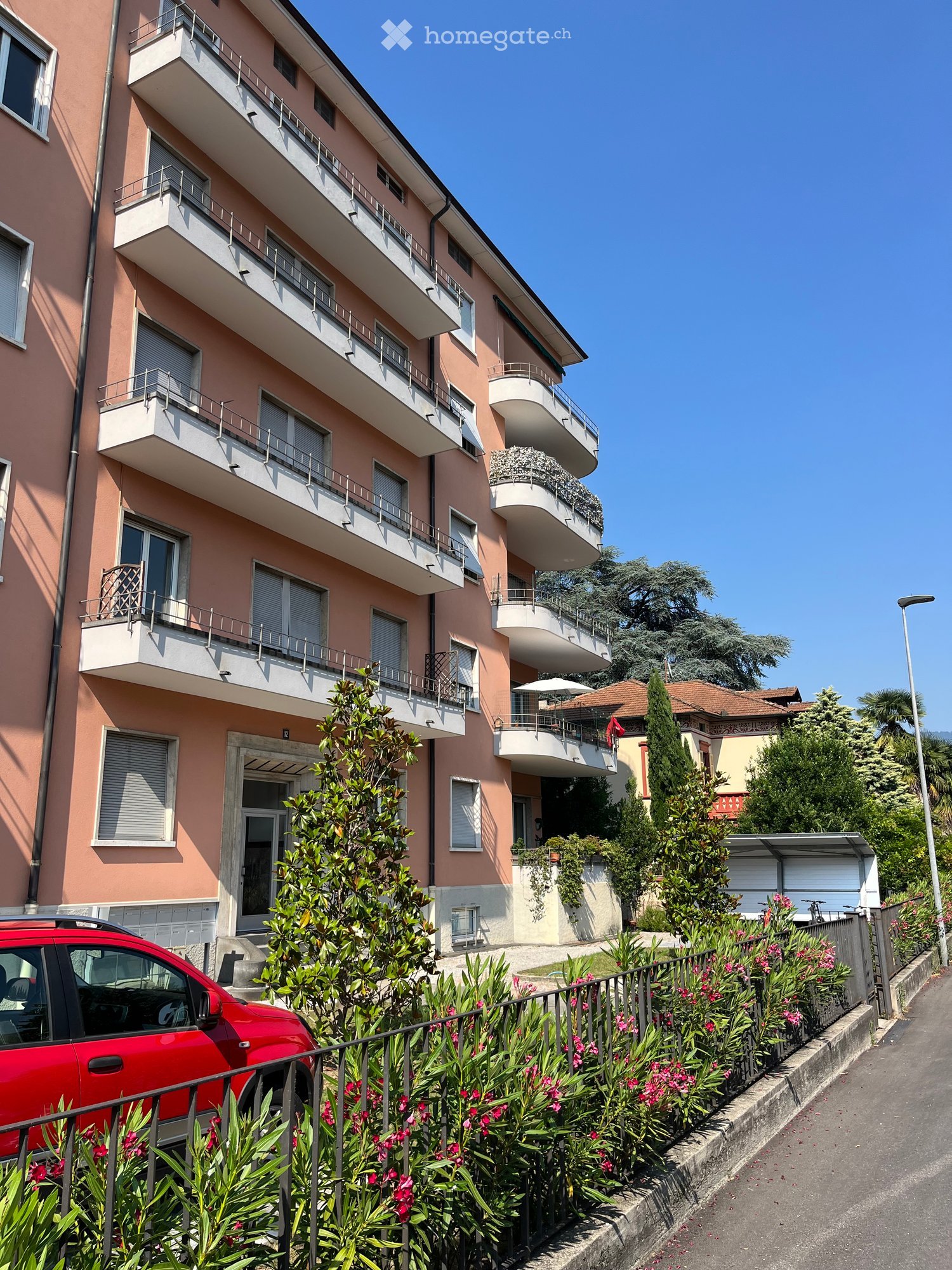 4 story building, pink exterior, multiple balconies, red car parked in front