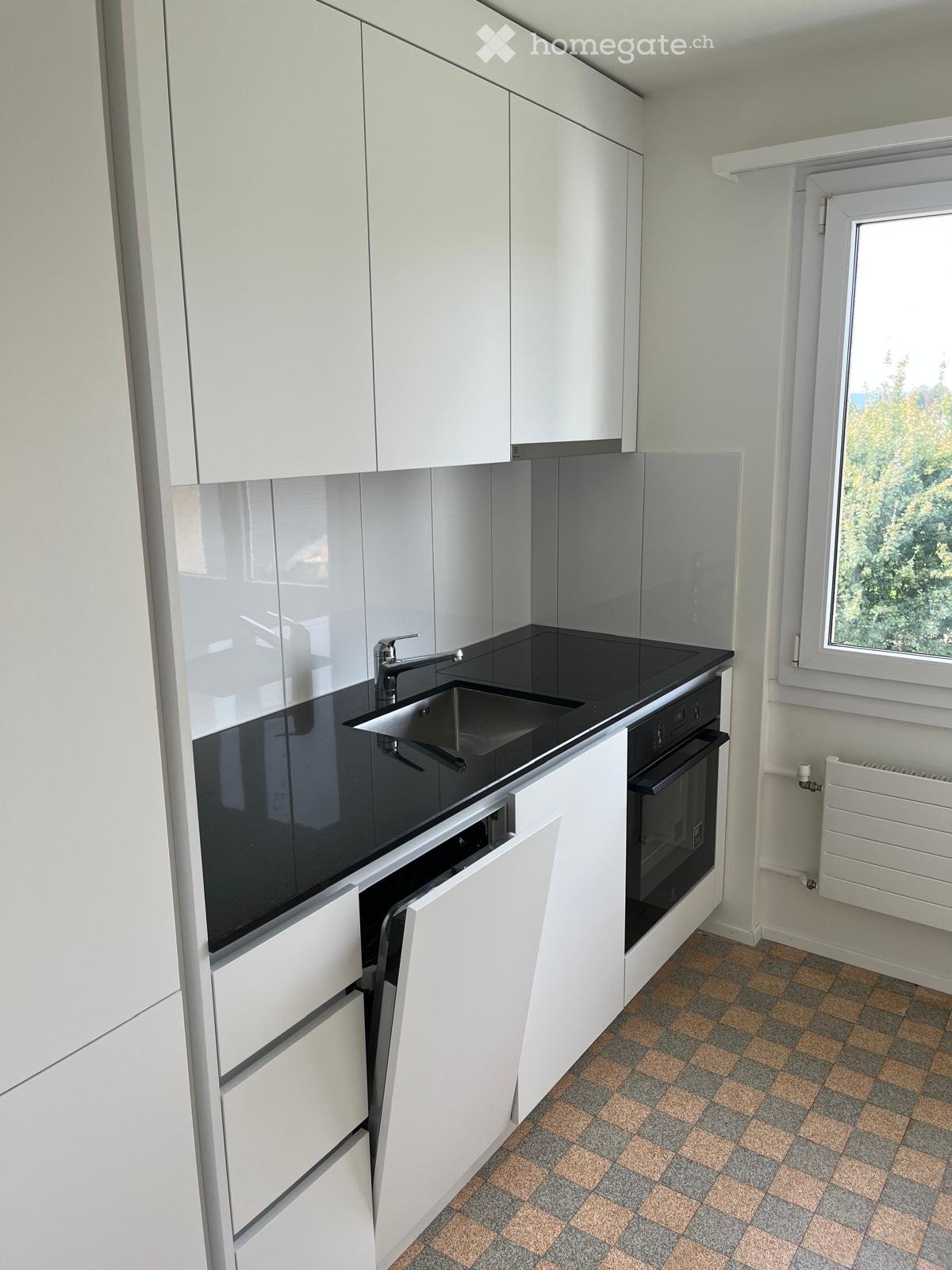 modern kitchen with white cabinets, black countertops, stainless steel sink, oven, dishwasher, and a window with a view