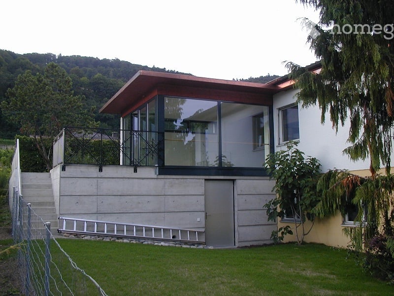 modern house, concrete walls, glass windows, balcony, metal railings, green lawn, trees