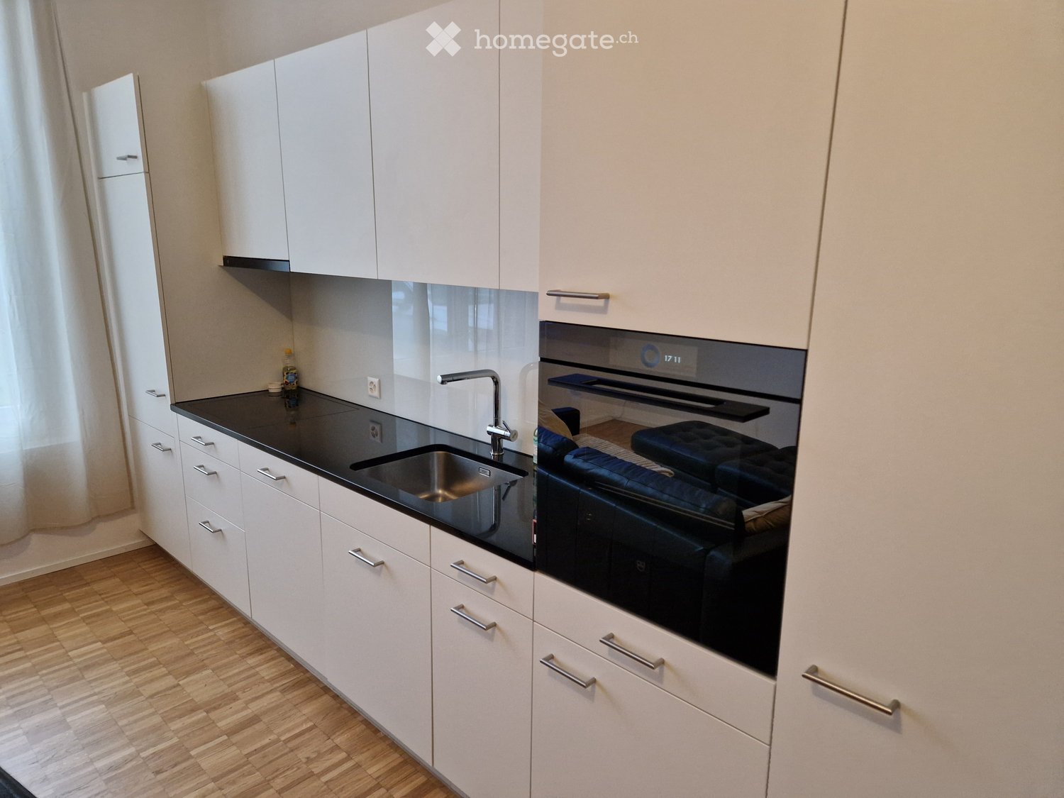 modern kitchen with white cabinets, black countertops, stainless steel sink, oven, wooden floor