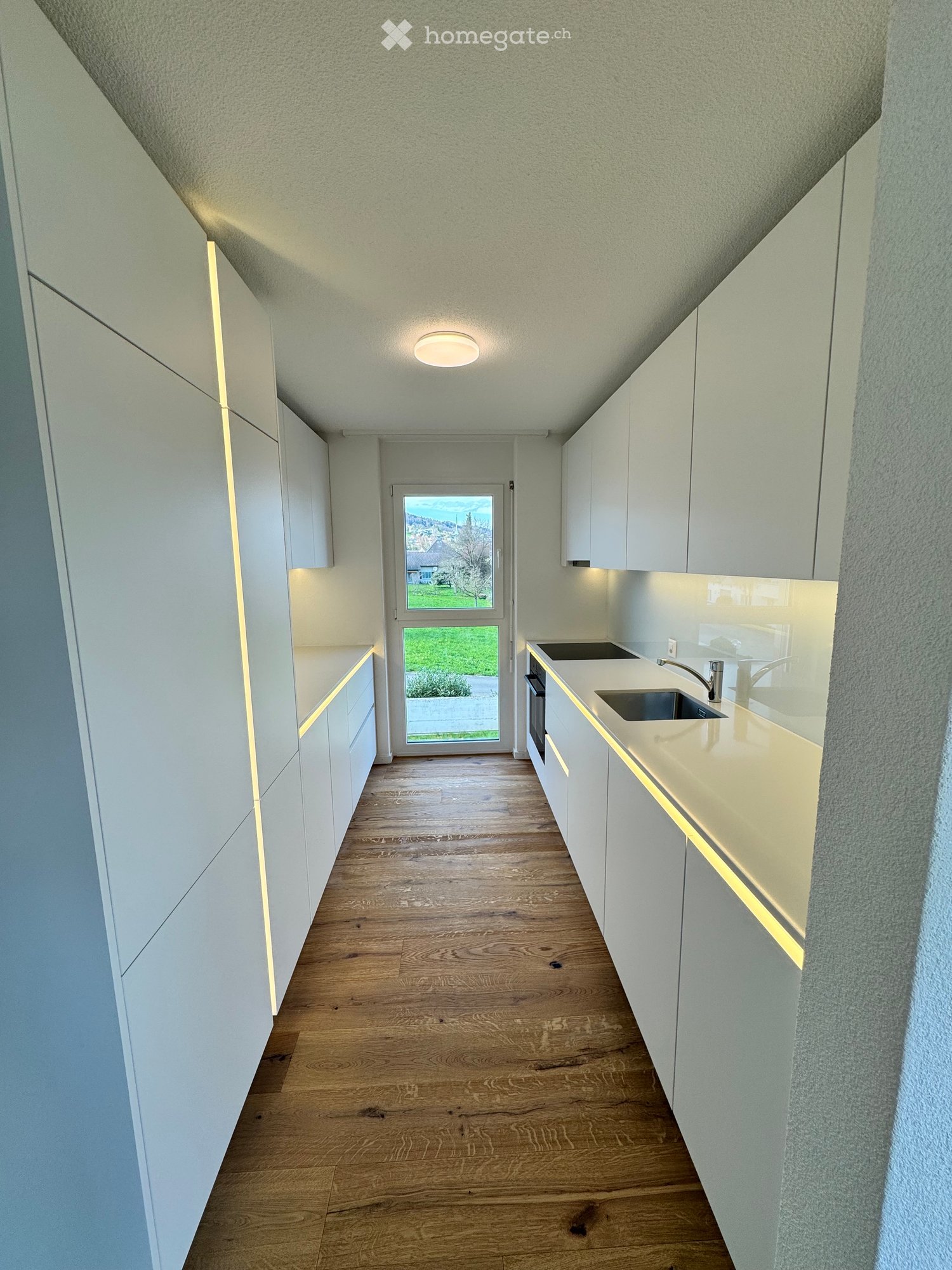 modern kitchen with white cabinets, wooden floor, sink, faucet, and a door leading to a grassy area