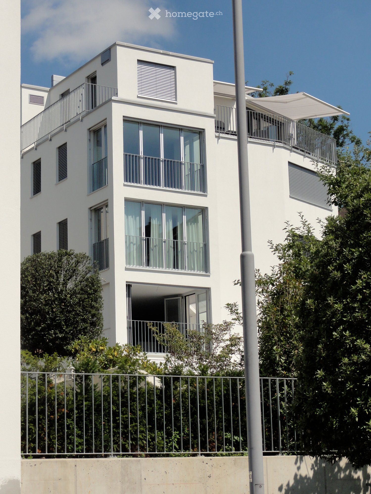 modern white apartment building, multiple balconies, glass facade, green surroundings