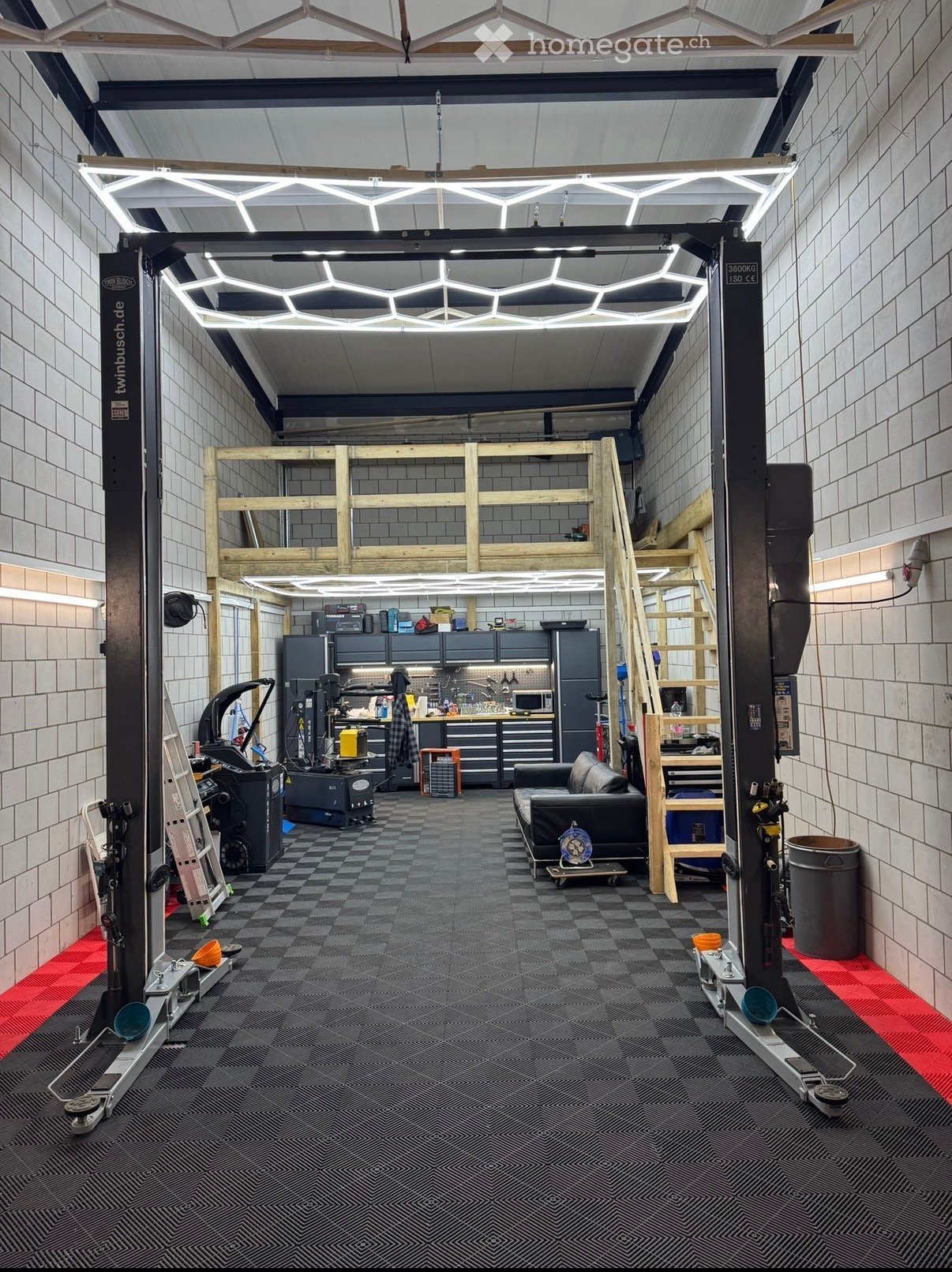 Garage with car lift, wooden stairs, tiled floor, brick walls, and various tools and equipment