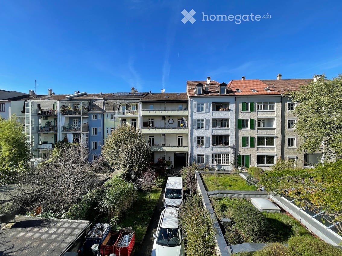 A multi-story building with several balconies, solar panels on the roof, and a garden in front.