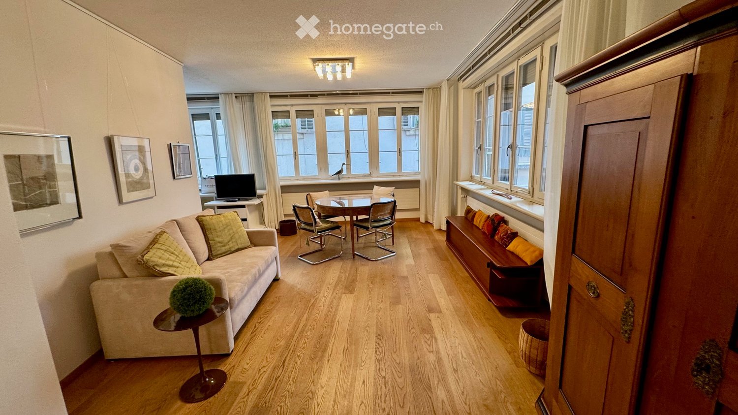 living room with couch, table, chairs, TV, wooden floor, windows, picture frames, wooden cabinet
