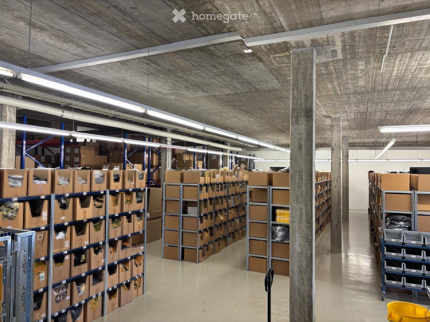Warehouse with multiple rows of storage boxes, metal shelves, and fluorescent lighting.
