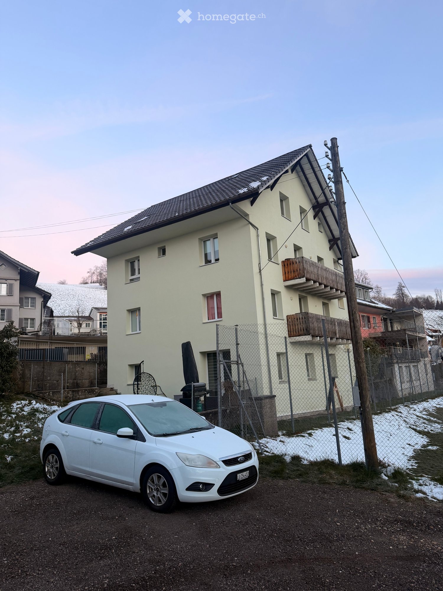3 story house, beige walls, black roof, balconies, fenced yard, snow on the ground