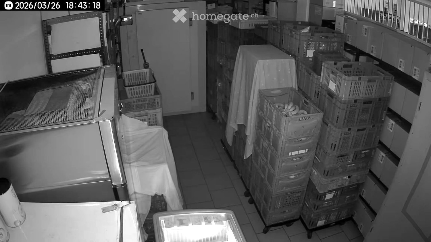 Storage room with stacked crates, covered table, and a refrigerator